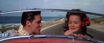 Movie still from “Blue Hawaii” (1961), directed by Norman Taurog – A man and a woman sitting in the back seat of a red car; Medium shot, Low angle