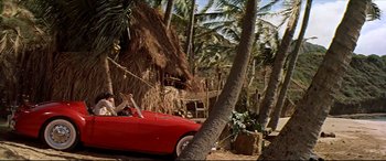 Movie still from “Blue Hawaii” (1961), directed by Norman Taurog – A man driving a red sports car through a palm tree filled forest; Wide shot, Low angle