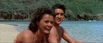 Movie still from “Blue Hawaii” (1961), directed by Norman Taurog – A man and a woman in the water at the edge of a body of water; Medium shot, Over the shoulder angle