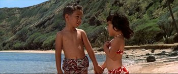 Movie still from “Blue Hawaii” (1961), directed by Norman Taurog – A young boy and a young girl holding hands on the beach; Medium shot, High angle