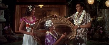 Movie still from “Blue Hawaii” (1961), directed by Norman Taurog – A woman holding a large basket while standing next to two other women; Medium shot, High angle