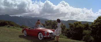 Movie still from “Blue Hawaii” (1961), directed by Norman Taurog – A man and a woman standing next to a red car; Extreme Wide shot, High angle
