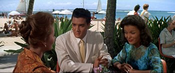 Movie still from “Blue Hawaii” (1961), directed by Norman Taurog – A man sitting at a table with two other people; Medium shot, Over the shoulder angle