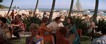 Movie still from “Blue Hawaii” (1961), directed by Norman Taurog – A group of people sitting at a table near the beach; Wide shot, High angle
