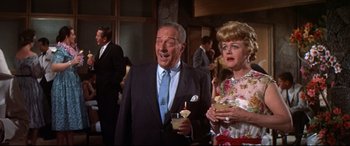 Movie still from “Blue Hawaii” (1961), directed by Norman Taurog – An older man and a woman standing next to each other holding drinks; Medium shot, Low angle