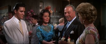 Movie still from “Blue Hawaii” (1961), directed by Norman Taurog – A man and a woman standing next to each other at a party; Medium shot, Low angle