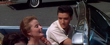 Movie still from “Blue Hawaii” (1961), directed by Norman Taurog – A man and a woman sitting next to each other on the side of the road; Medium shot, Over the shoulder angle