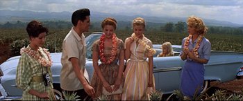 Movie still from “Blue Hawaii” (1961), directed by Norman Taurog – Two women and a man standing in front of a car; Wide shot, Over the shoulder angle