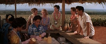 Movie still from “Blue Hawaii” (1961), directed by Norman Taurog – A group of people standing around a table; Medium shot, Low angle