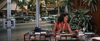 Movie still from “Blue Hawaii” (1961), directed by Norman Taurog – A woman sitting at a table with a lot of books; Medium shot, Over the shoulder angle