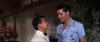Movie still from “Blue Hawaii” (1961), directed by Norman Taurog – A man standing next to another man in a room; Medium shot, Low angle