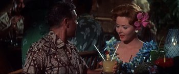 Movie still from “Blue Hawaii” (1961), directed by Norman Taurog – A man and a woman holding a drink in a tiki bar; Medium shot, Over the shoulder angle