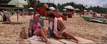 Movie still from “Blue Hawaii” (1961), directed by Norman Taurog – A man and a woman sitting on the beach with surfboards in the background; Wide shot, High angle