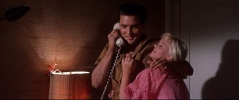 Movie still from “Blue Hawaii” (1961), directed by Norman Taurog – A man talking on a phone next to a woman; Medium shot, Low angle