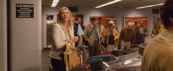 Movie still from “Blue Jasmine” (2013), directed by Woody Allen – A group of people standing in a line at a baggage claim area; Medium shot, Over the shoulder angle