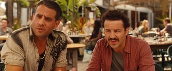 Movie still from “Blue Jasmine” (2013), directed by Woody Allen – Two men sitting at a table in front of some people; Close Up shot, Over the shoulder angle