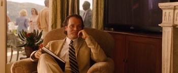 Movie still from “Blue Jasmine” (2013), directed by Woody Allen – A man sitting in a chair holding a book and wearing a suit; Medium shot, Over the shoulder angle