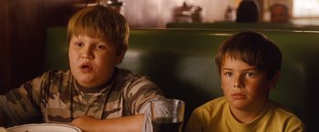 Movie still from “Blue Jasmine” (2013), directed by Woody Allen – Two young boys sitting at a table with a glass of beer; Medium shot, Low angle
