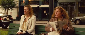 Movie still from “Blue Jasmine” (2013), directed by Woody Allen – Two women are sitting on a bench and one of them is reading a newspaper; Medium shot, Over the shoulder angle