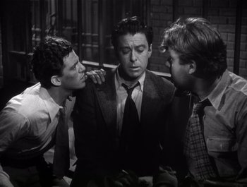 Movie still from “Blues in the Night” (1941), directed by Anatole Litvak – Three men in suits and ties , one of which has his hand on the shoulder of another man; Medium shot, Over the shoulder angle