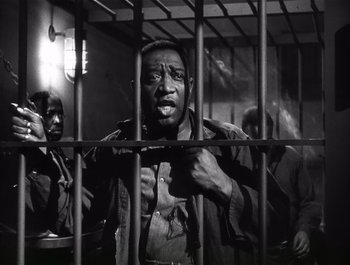 Movie still from “Blues in the Night” (1941), directed by Anatole Litvak – A black and white photo of a man behind bars; Medium shot, Low angle
