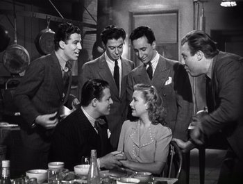 Movie still from “Blues in the Night” (1941), directed by Anatole Litvak – A group of men standing around a woman in front of a table; Medium shot, Low angle