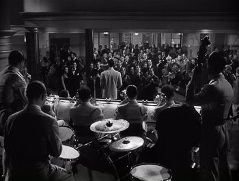 Movie still from “Blues in the Night” (1941), directed by Anatole Litvak – A group of people sitting in a room with drums; Extreme Wide shot, High angle