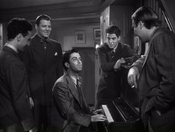 Movie still from “Blues in the Night” (1941), directed by Anatole Litvak – A group of men standing around a man playing a piano; Medium shot, High angle