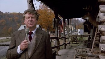 Movie still from “Bob Roberts” (1992), directed by Tim Robbins – A man wearing a suit and tie holding a microphone; Medium shot, Low angle