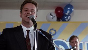 Movie still from “Bob Roberts” (1992), directed by Tim Robbins – A man wearing a suit and tie is speaking into a microphone; Close Up shot, Low angle