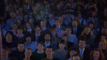 Movie still from “Bob Roberts” (1992), directed by Tim Robbins – A large group of people sitting in a room; Wide shot, High angle