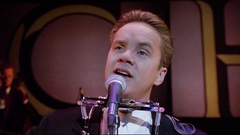 Movie still from “Bob Roberts” (1992), directed by Tim Robbins – A man in a tuxedo is singing into a microphone; Close Up shot, Low angle