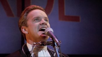 Movie still from “Bob Roberts” (1992), directed by Tim Robbins – A man in a tuxedo is singing into a microphone; Close Up shot, Low angle