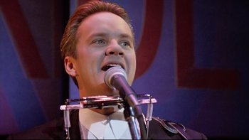 Movie still from “Bob Roberts” (1992), directed by Tim Robbins – A man is singing into a microphone on a stage; Close Up shot, Low angle