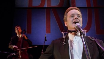Movie still from “Bob Roberts” (1992), directed by Tim Robbins – A man in a suit and tie singing into a microphone; Close Up shot, Low angle