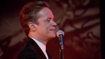 Movie still from “Bob Roberts” (1992), directed by Tim Robbins – A man in a black suit is singing into a microphone; Close Up shot, Low angle