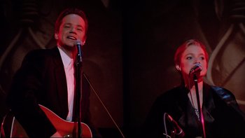Movie still from “Bob Roberts” (1992), directed by Tim Robbins – A man and a woman singing into microphones; Medium shot, Low angle