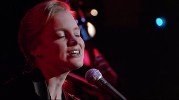 Movie still from “Bob Roberts” (1992), directed by Tim Robbins – A woman singing into a microphone on a stage; Close Up shot, Low angle