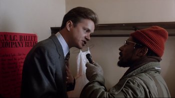 Movie still from “Bob Roberts” (1992), directed by Tim Robbins – Two men in a suit and tie one of which is holding a microphone and the other is holding a microphone; Close Up shot, Low angle