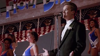 Movie still from “Bob Roberts” (1992), directed by Tim Robbins – A man and a woman standing next to each other on a stage with microphones; Medium shot, Low angle