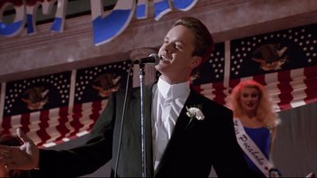 Movie still from “Bob Roberts” (1992), directed by Tim Robbins – A man in a tuxedo singing into a microphone; Medium shot, Low angle