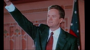 Movie still from “Bob Roberts” (1992), directed by Tim Robbins – A person wearing a suit and tie; Medium shot, Low angle