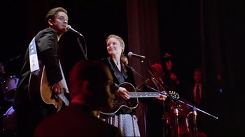 Movie still from “Bob Roberts” (1992), directed by Tim Robbins – A man and a woman singing on a stage; Medium shot, Low angle