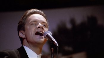 Movie still from “Bob Roberts” (1992), directed by Tim Robbins – A man in a white shirt is singing into a microphone; Close Up shot, Low angle