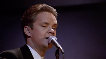 Movie still from “Bob Roberts” (1992), directed by Tim Robbins – A man in a black suit is singing into a microphone; Close Up shot, Low angle
