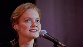 Movie still from “Bob Roberts” (1992), directed by Tim Robbins – A young woman is holding a microphone up to her face; Close Up shot, Low angle