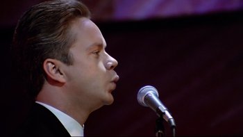 Movie still from “Bob Roberts” (1992), directed by Tim Robbins – A person speaking on a microphone; Close Up shot, Low angle