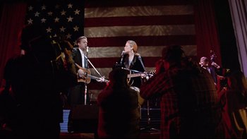 Movie still from “Bob Roberts” (1992), directed by Tim Robbins – A man and a woman are singing on a stage; Wide shot, Low angle