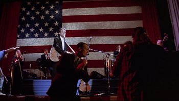Movie still from “Bob Roberts” (1992), directed by Tim Robbins – A group of people standing in front of an american flag; Wide shot, Low angle