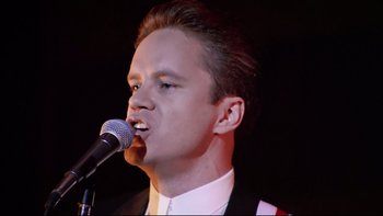 Movie still from “Bob Roberts” (1992), directed by Tim Robbins – A man in a suit is singing into a microphone; Close Up shot, Low angle
